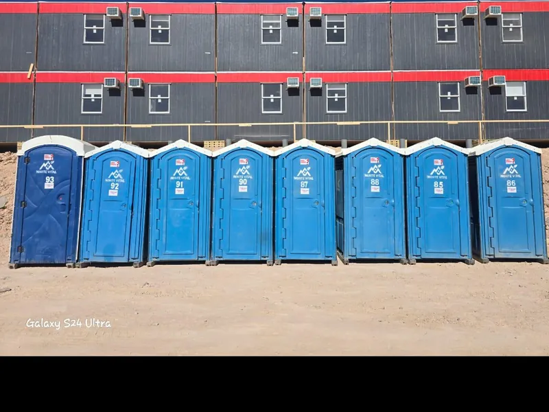 Fila de ocho baños químicos de Norte Vital instalados frente a un campamento modular minero