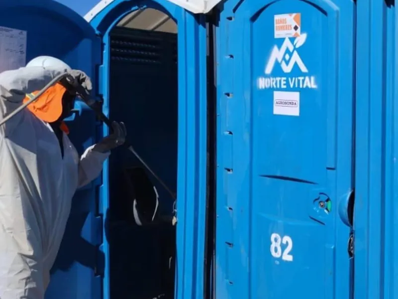 Operador con traje de protección sanitizando el interior de un baño químico con hidrolavadora